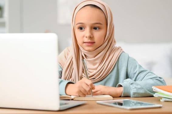 Malá muslimská dievčatko robí domácu úlohu doma v hidžábe.