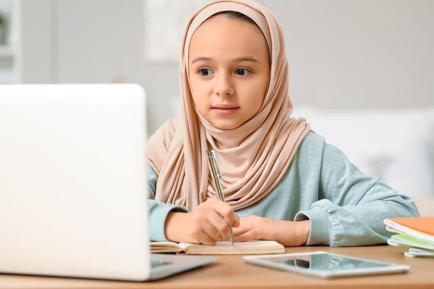 Malá muslimská dievčatko robí domácu úlohu doma v hidžábe.