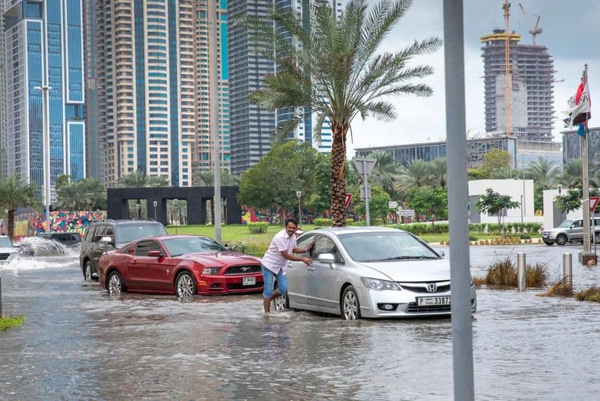 Ľudia tlačiaci autá z vody na zaplavených uliciach v Dubaji.