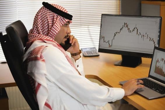 Arab pracujúci na notebooku v kancelárii, sledujúci burzový trh