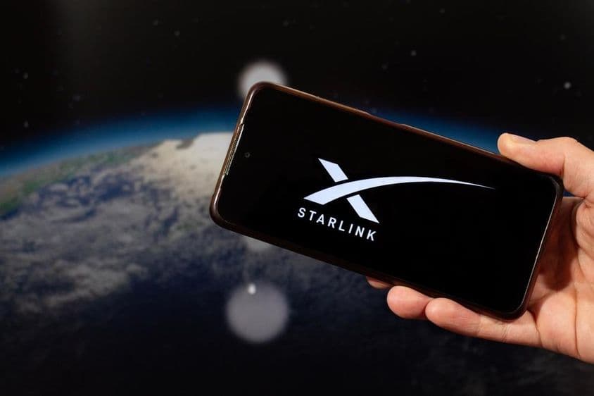 Mužská ruka držiaca smartfón s logom Starlink v pravej ruke.