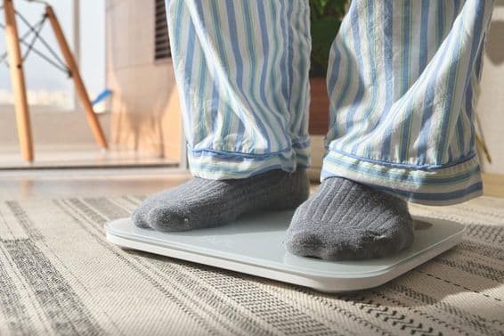 Muž v pruhovanej pyžame stojací na bielej digitálnej váhe