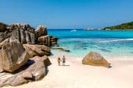 Dvaja cestovatelia kráčajúci po mäkkých bielych pieskoch pláže Anse Cocos na Seycheloch.