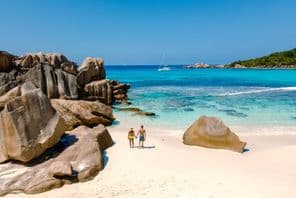 Dvaja cestovatelia kráčajúci po mäkkých bielych pieskoch pláže Anse Cocos na Seycheloch.