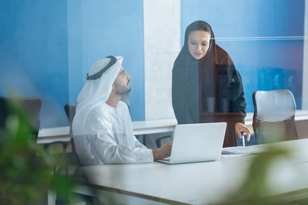 Muž a žena v tradičnom odeve pracujúci v obchodnej kancelárii v Dubaji.