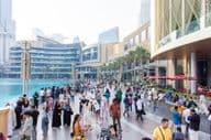 Pestrý dav turistov a miestnych prechádza rušnou nábrežnou promenádou pred Dubai Mall.