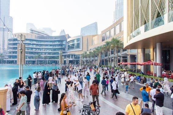 Pestrý dav turistov a miestnych prechádza rušnou nábrežnou promenádou pred Dubai Mall.